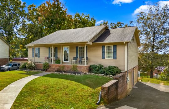 ranch style home, front yard, sidewalk, driveway, two car drive-under garage, back yard, vinyl siding, covered front porch, front door, landscaping, shingle roof