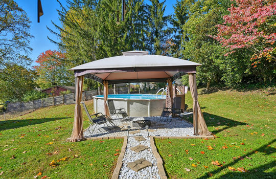 outdoor seating area, gravel, back yard, above ground swimming pool, fencing, trees