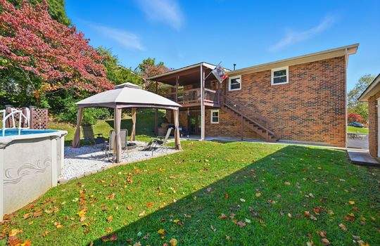 back yard, back of home, brick exterior, lower level patio, covered back deck, back yard, seating area, above ground pool, fencing, trees