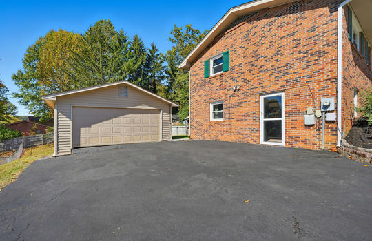 driveway, detached garage, lower level entry door, side view of home, brick exterior