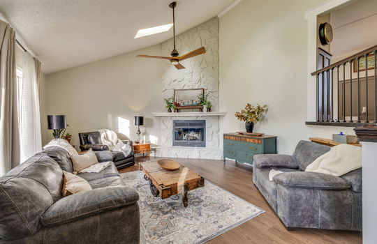 living room, luxury vinyl flooring, painted stone fireplace, ceiling fan, vaulted ceiling, windows, skylight