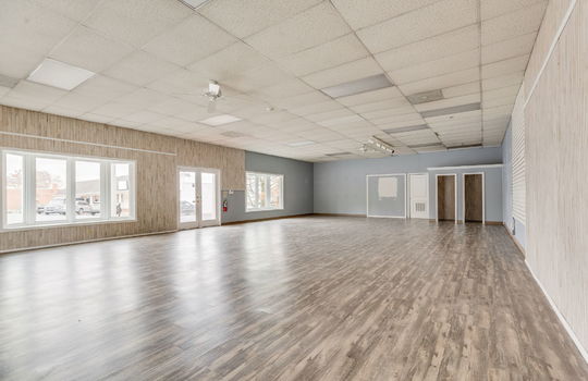 interior of commercial space toward front doors, commercial building for lease, vinyl flooring, ceiling tiles, fluorescent lighting, closets/changing rooms.