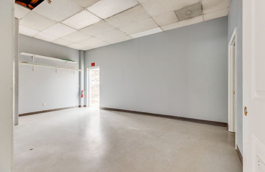 Private office space or employee break room, tile flooring, Ceiling tiles, fluorescent lighting, back entry/employee exit door, storage shelves