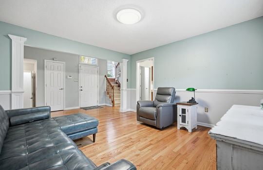 living room view toward front door, stairs to upper level, hardwood flooring, doorway to kitchen