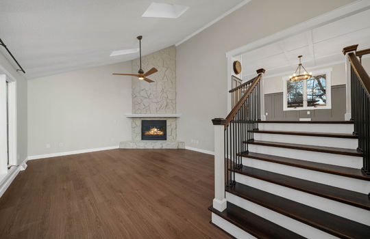 living room, stairs to upper level, luxury vinyl flooring, ceiling fan, skylights, windows, painted stone fireplace