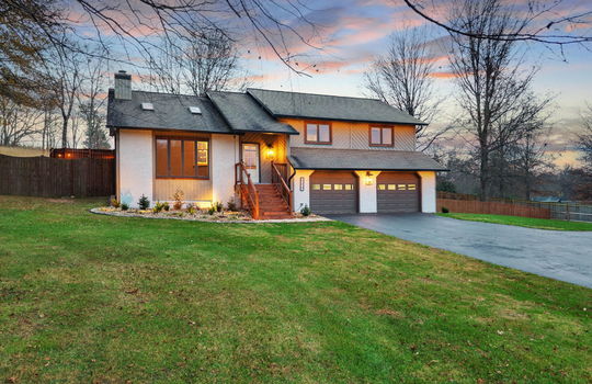 twilight photo, yard, driveway, two car garage, landscaping, contemporary home, wood siding, brick exterior, fencing, stairs to front door, front door