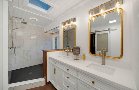 primary bathroom, skylight, window, shower, tile shower surround, bathroom vanity, double sink vanity, luxury vinyl flooring