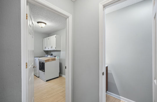 hallway view into bathroom and laundry area, tile flooring, cabinets