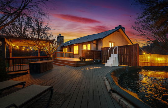twilight photo of back deck, pool, pergola, back of home, wood siding
