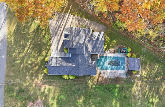 overhead aerial view of home, roof, swimming pool, front yard, back yard, driveway, fencing, trees, road