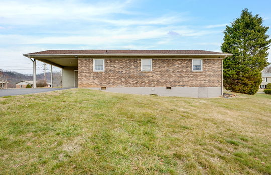 back of home, crawl space door, carport, driveway, brick exterior, ranch home