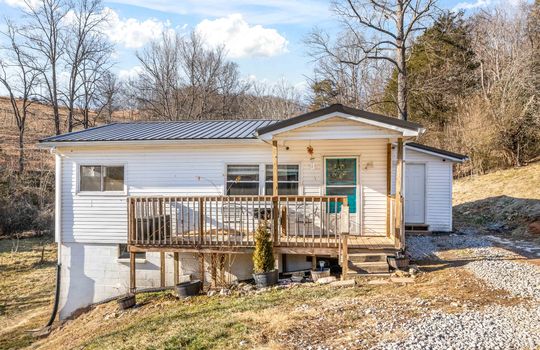 house, vinyl siding, covered front porch, front door, gravel driveway, trees