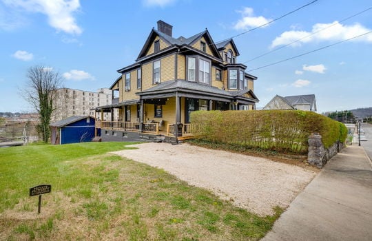 left side view of home, Victorian Home, covered porch, wrap around porch, wood siding, driveway, gravel driveway, sidewalk, hedge