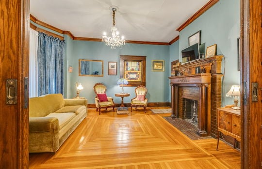 formal living room, hardwood flooring, wood trim, chandelier, wood fireplace mantle, fireplace, bay window