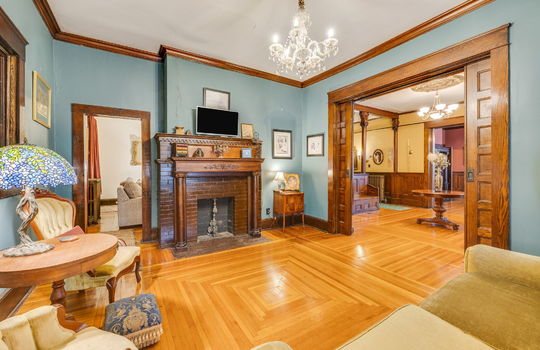 formal living room, fireplace, wood mantle, hardwood flooring, pocket doors, wood pocket doors, wood trim, chandelier, doorway to foyer, doorway to other room,