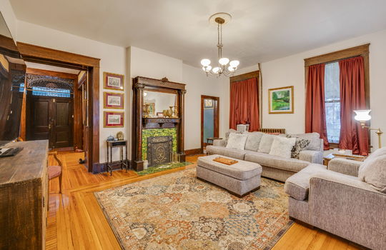 den, doorway to foyer, hardwood flooring, mirrored mantle, fireplace, tile surround on fireplace, windows, chandelier, wood trim, hardwood flooring