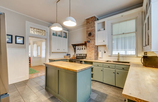 kitchen, kitchen island, butcher block countertops, transom window, cabinets, brick chimney feature, sink, range, refrigerator, windows