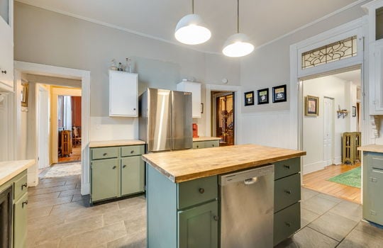 kitchen, transom window, doorways, stainless steel appliances, kitchen island with dishwasher, cabinets, butcher block countertops, tile flooring, pendant lights