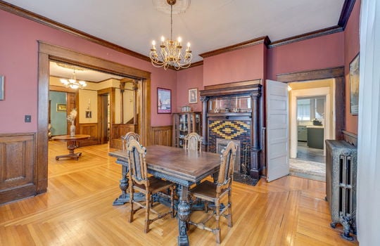 formal dining room, hardwood flooring, radiator, fireplace, tile surround on fireplace, wood mantle, pocket doors, wood wainscoting, chandelier, doorways to kitchen and foyer