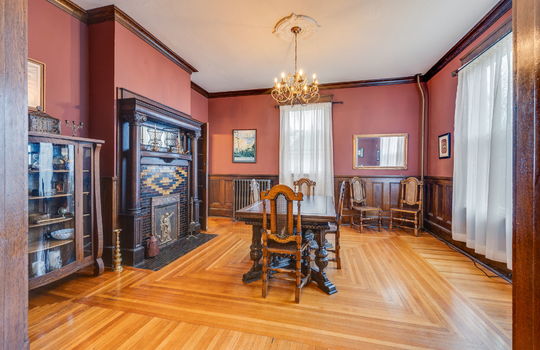 foyer view of formal dining room, fireplace with tile and wood mantle, hardwood flooring, windows, wood wainscoting, radiator