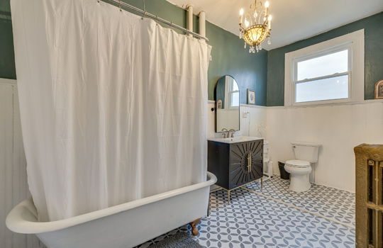 primary bathroom, claw foot tub with shower, sink, toilet, window, tile flooring, radiator, chandelier