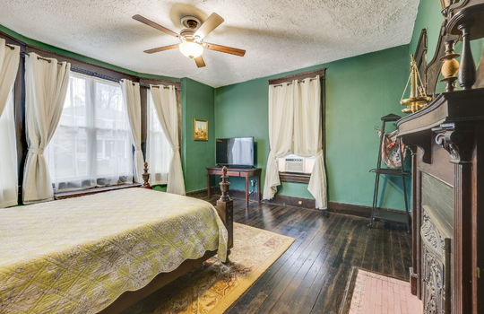 bedroom, bay window, bench seat, windows, hardwood flooring, fireplace, tile surround on fireplace, wood mantle, wood trim, ceiling fan