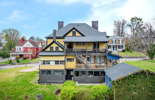aerial view of back of home, wood siding, porches/balcony, covered porches, yard, nearby homes, storage shed