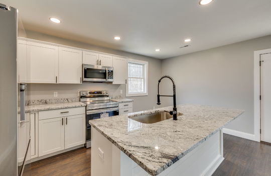kitchen, cabinets, countertops, island, sink in island, stainless appliances, refrigerator, range, built in microwave, recessed lighting, window, door
