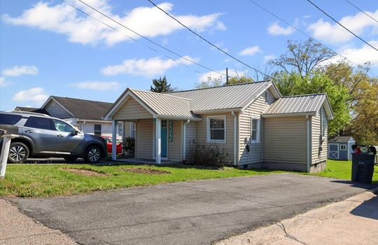 cottage, front view of home, second driveway, vinyl siding, metal roof, covered front porch, front door, front yard