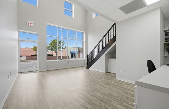 interior view toward front of building, large windows, glass entry door, luxury vinyl flooring, fluorescent lighting, stairs to upper level