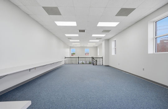 upper level view toward front of building, carpet, built-in desk units, windows, stairs, banister, fluorescent lighting