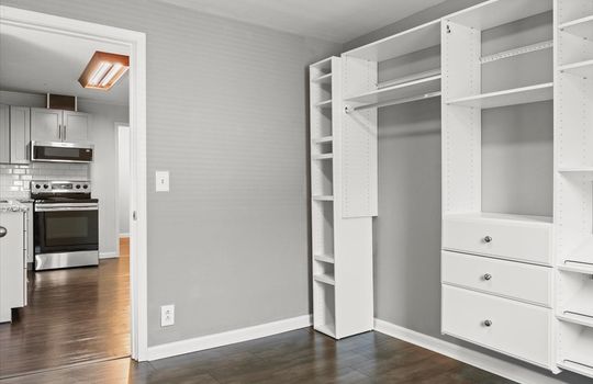 second bedroom, door to kitchen, storage shelving, vinyl flooring