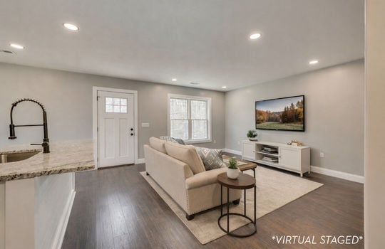 virtually staged photo of living room area, kitchen, exterior door, recessed lighting
