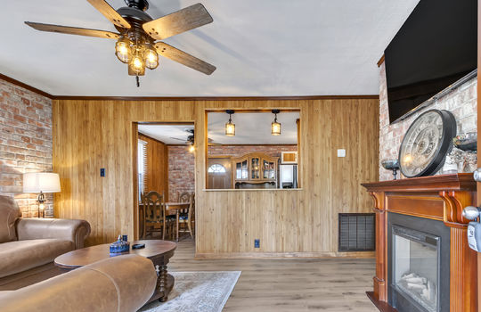 living room, paneling walls, cut out to view into kitchen/dining area, doorway, ceiling fan, laminate flooring, brick feature wall