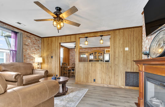 living room, paneling walls, cut out to view into kitchen/dining area, doorway, ceiling fan, laminate flooring, brick feature wall