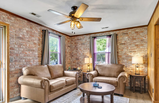 living room, brick walls, laminate flooring, windows, ceiling fan, front door