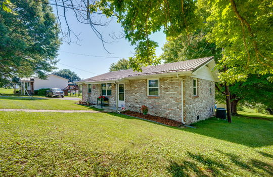 right side view of home, brick, ranch style home, covered front porch, front door, metal roof, front yard, sidewalk