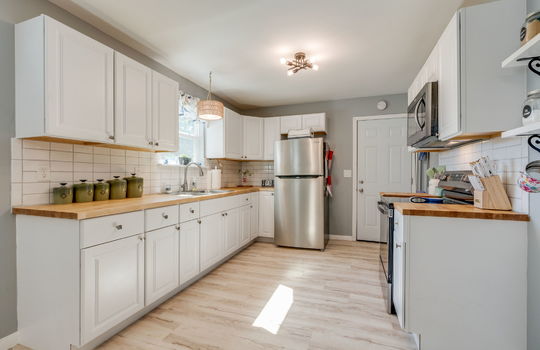 kitchen, butch block countertops, cabinets, tile backsplash, sink, stainless appliances, luxury vinyl flooring, sink, window above sink, refrigerator, electric range, builtin microwave
