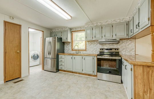 kitchen, door to laundry space, pantry door, vinyl flooring, cabinets, countertops, window above sink, sink, refrigerator, electric range, tile backsplash