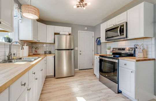 kitchen, butcher block countertops, cabinets, stainless appliances, refrigerator, built-in microwave, electric range, tile backsplash, luxury vinyl flooring, sink, window above sink