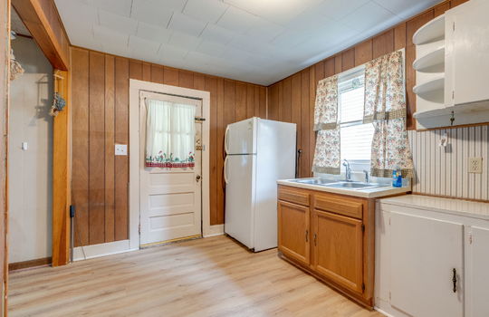 kitchen, exterior door, paneling walls, refrigerator, sink, window above sink, cabinets, countertops, laminate flooring