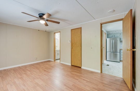 primary bedroom, closet, ceiling fan, doorway to kitchen, laminate flooring, doorway to primary bathroom
