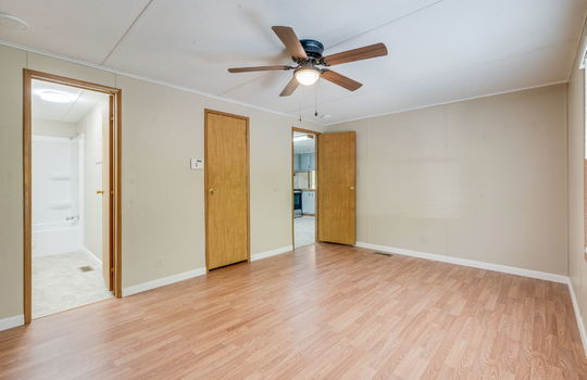 primary bedroom, doorway to primary bathroom, closet, doorway to kitchen, ceiling fan, laminate flooring