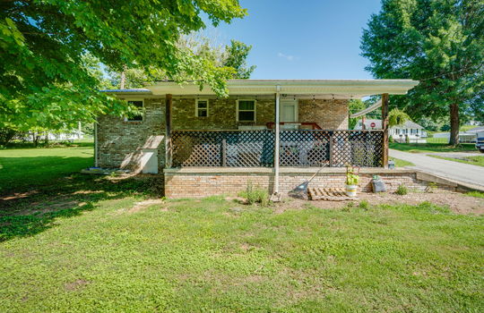 back of home, brick, ranch style home, parking pad, covered back porch, exterior door, back yard