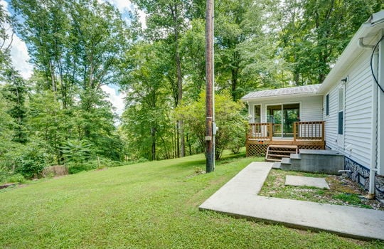 back of home, sidewalk, stairs to back exterior entry, stairs to back porch/sunroom, back yard, trees, vinyl siding, metal roof