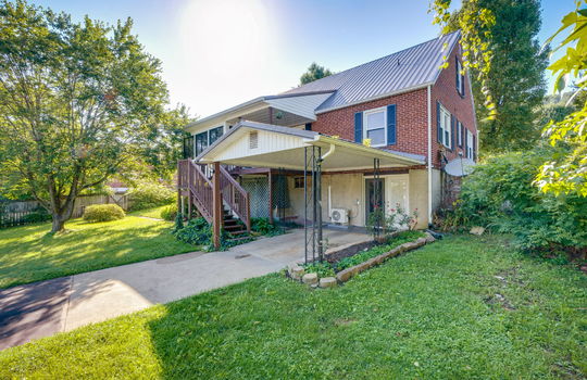 back of home, carport, stairs to back porch, sunroom, exterior entry doors, landscaping, fencing, back yard, metal roof