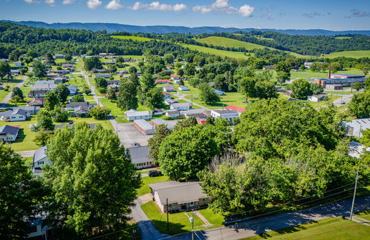 aerial view of home, metal roof, front yard, trees, nearby homes and businesses, mountains