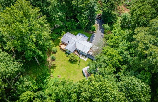 aerial view of property, metal roof, front yard, back yard, storage sheds, back porch, covered front porch, driveway, trees