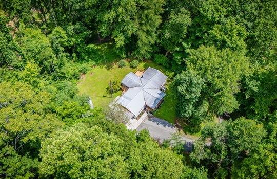 aerial view of property, metal roof, front yard, back yard, storage sheds, back porch, covered front porch, driveway, trees
