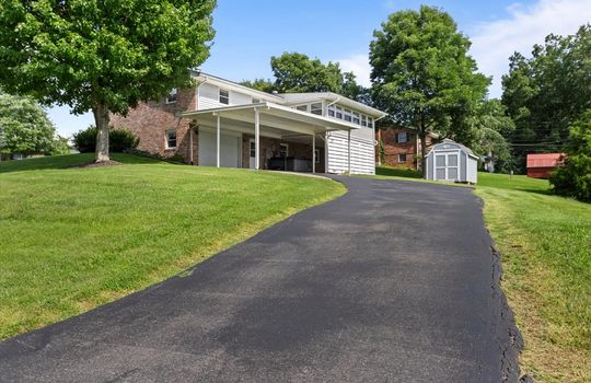 driveway, carport, garage, garage door, patio, sunroom, brick exterior, yard, trees, neighboring homes, storage shed